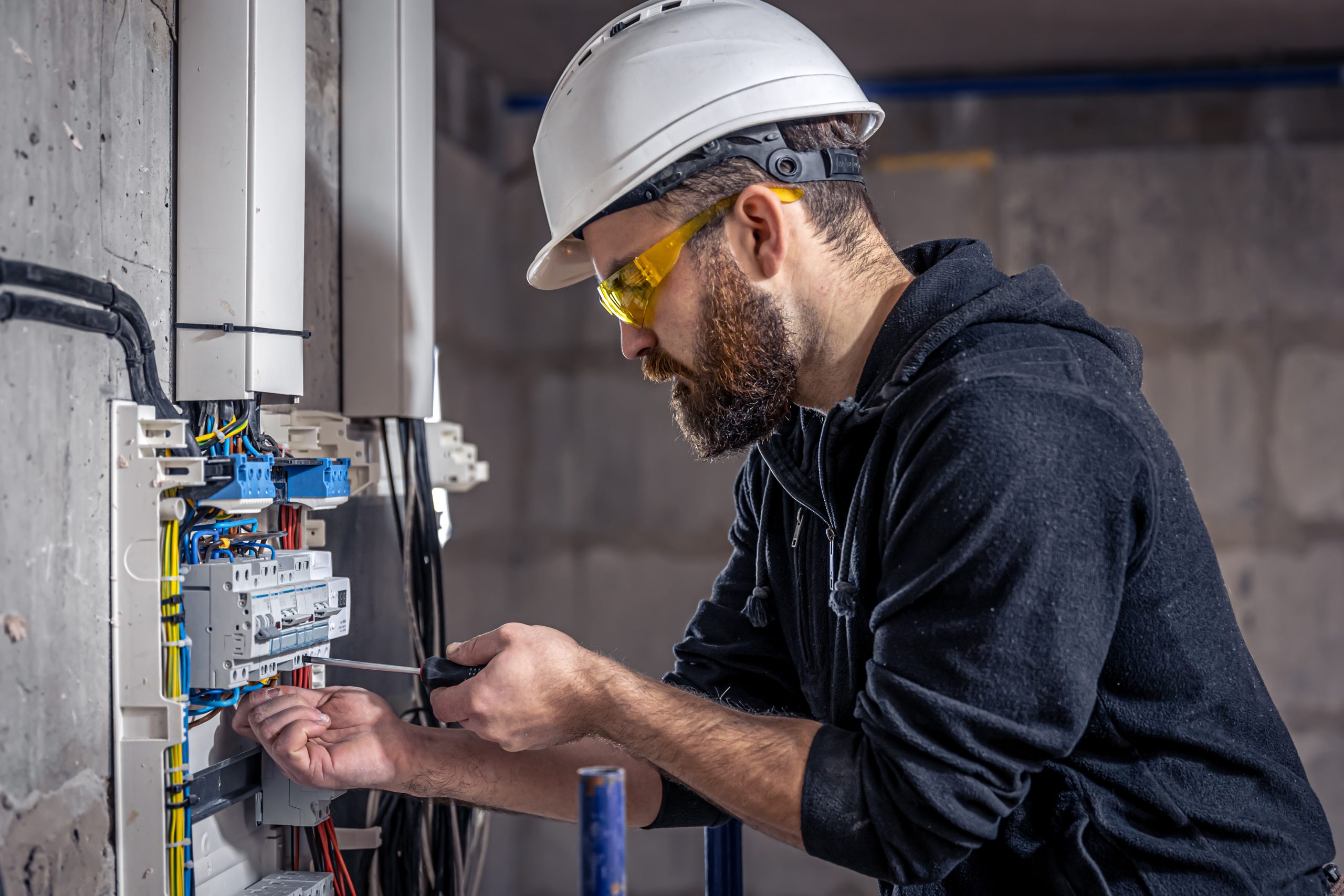A male electrician works in a switchboard with an electrical connecting cable.